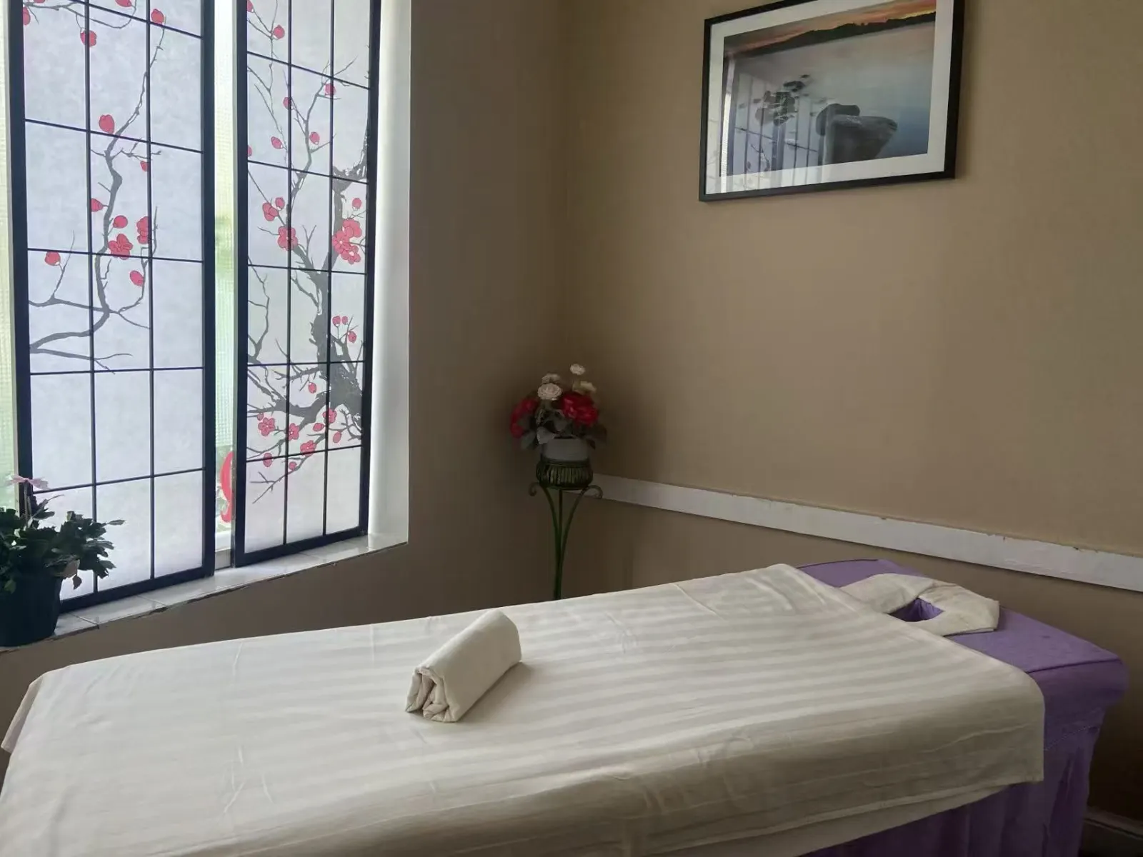 Treatment room with a massage table beside a window with cherry blossom screens